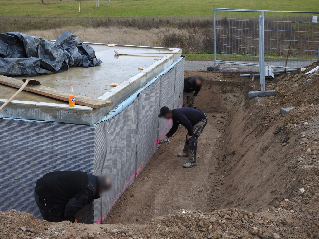 Kelleransicht mit drei Arbeitern, die eine Höhe für die Verlegung der Regenabwasserrohre markieren.